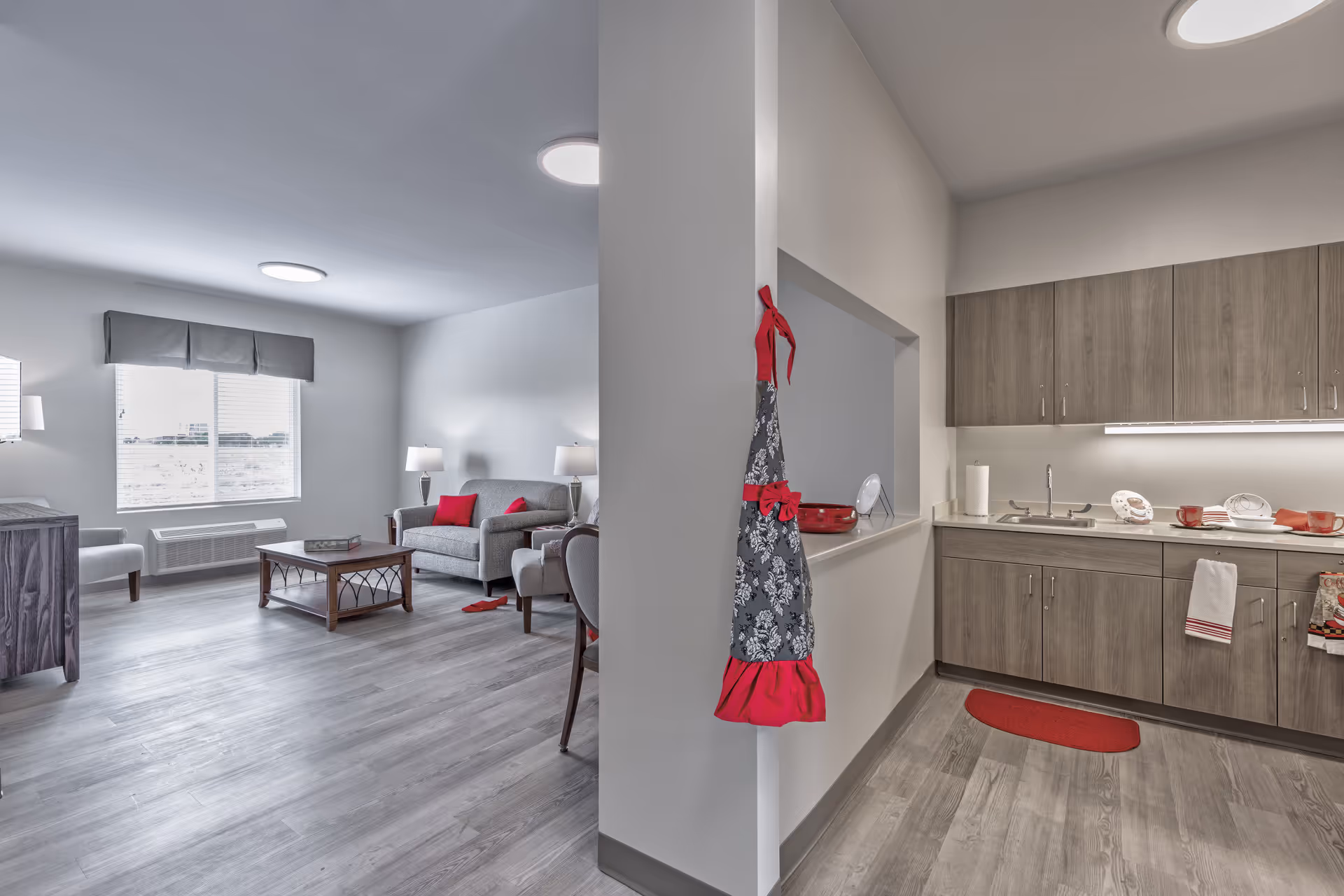Open-plan senior apartment interior with a living area (sofa, coffee table) and a kitchenette separated by a half wall.