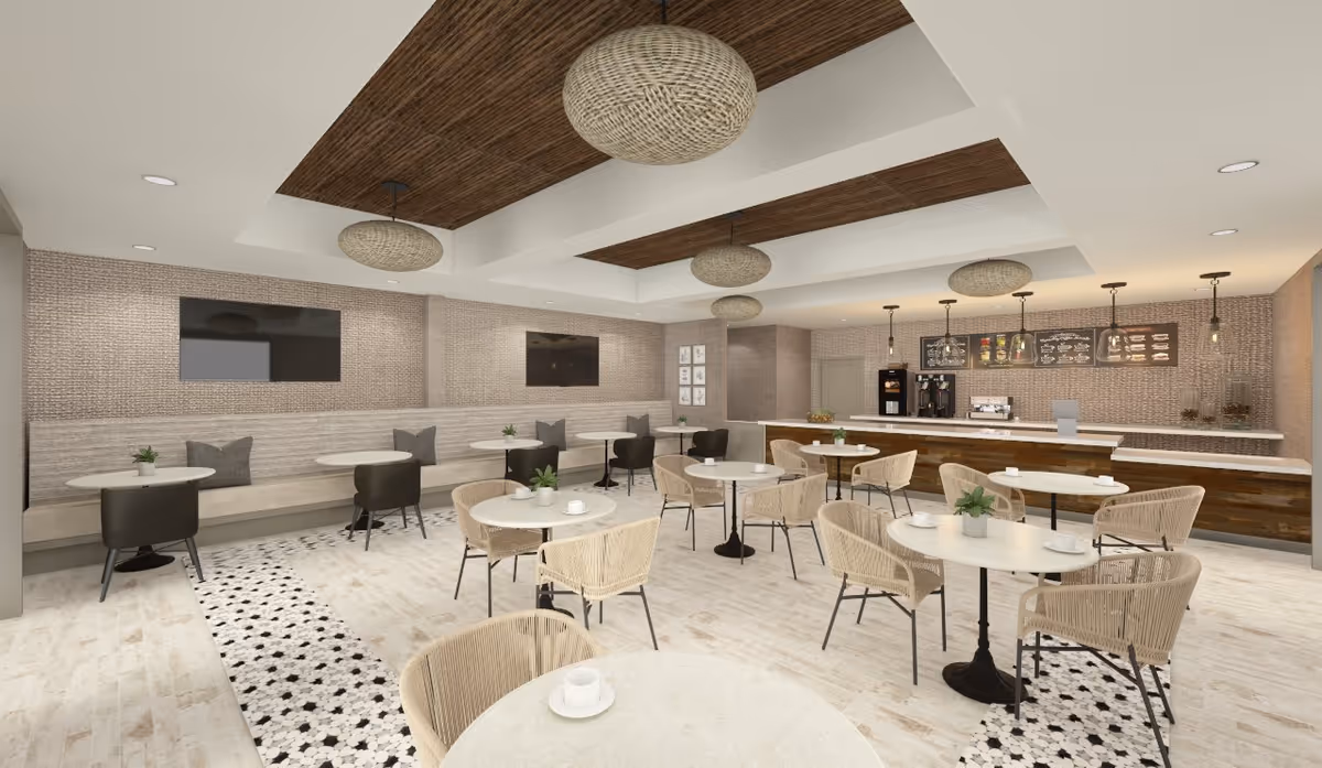 A modern dining area with round tables and wicker chairs, a long bench with cushions along the wall, two large flat-screen TVs mounted on the wall, pendant lights hanging from a ceiling with wooden accents, and a counter area with coffee machines and menu boards in the background.