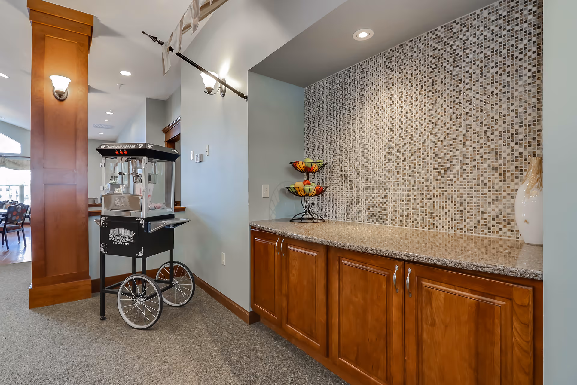 Interior serving area with a popcorn cart next to wooden cabinets and a mosaic-tiled countertop.