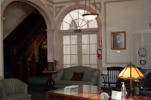 A formal sitting area with couches, a coffee table, a wooden staircase, and arched glass doors.