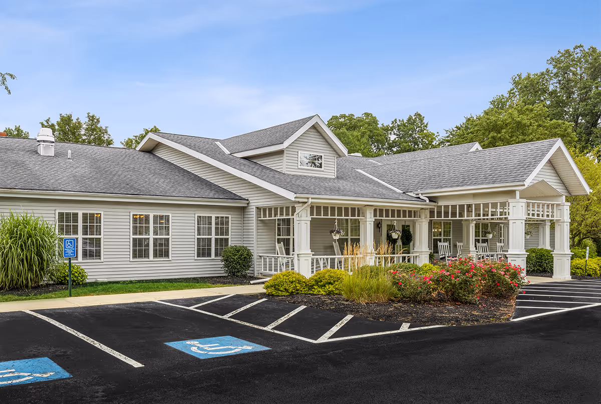 White bungalow-style senior living facility with a wide porch, landscaping, and accessible parking.