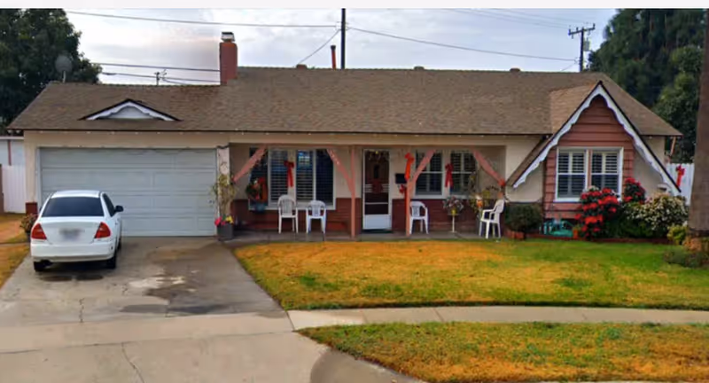 A single-story house with a decorated front porch, white chairs, and a parked car.