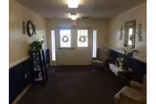 Interior view of an assisted living facility entrance area with double doors decorated with wreaths, a bench, a small table with plants, a mirror on the wall, and a shelf with decorative items.