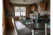 Open kitchen and dining area with wooden cabinets, a central table/island set with placemats and chairs, and a large window.