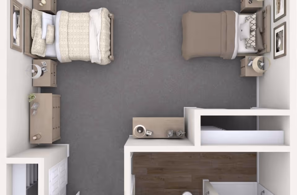 Top-down view of a room layout with two single beds, each with pillows and blankets. There are nightstands with lamps beside each bed, a dresser with decorative items, and a small table with a lamp and other items. The room has carpeted flooring and an adjacent area with wood flooring that appears to be a bathroom.