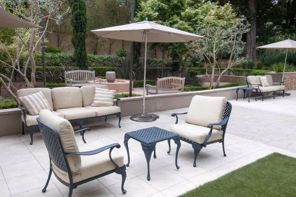 Outdoor patio with cushioned chairs, sofas, umbrellas and landscaped greenery.