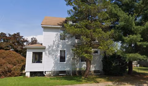 Two-story white house exterior with trees and a grassy yard, no people present.
