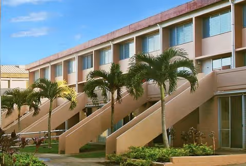 Exterior view of a senior living facility with beige staircases and palm trees.