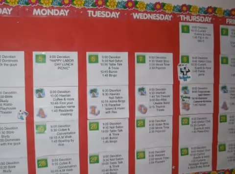 Red activity bulletin board showing a weekly schedule with days of the week and small printed event cards.