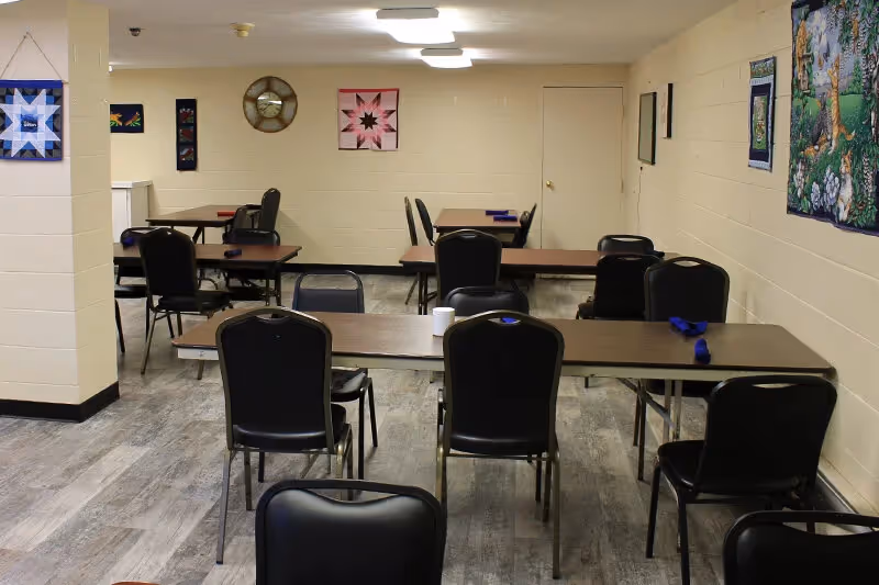 A room with multiple tables and black chairs in a communal dining area.