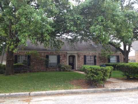Brick cottage-style building with a manicured lawn, trees, and shrubs in front.