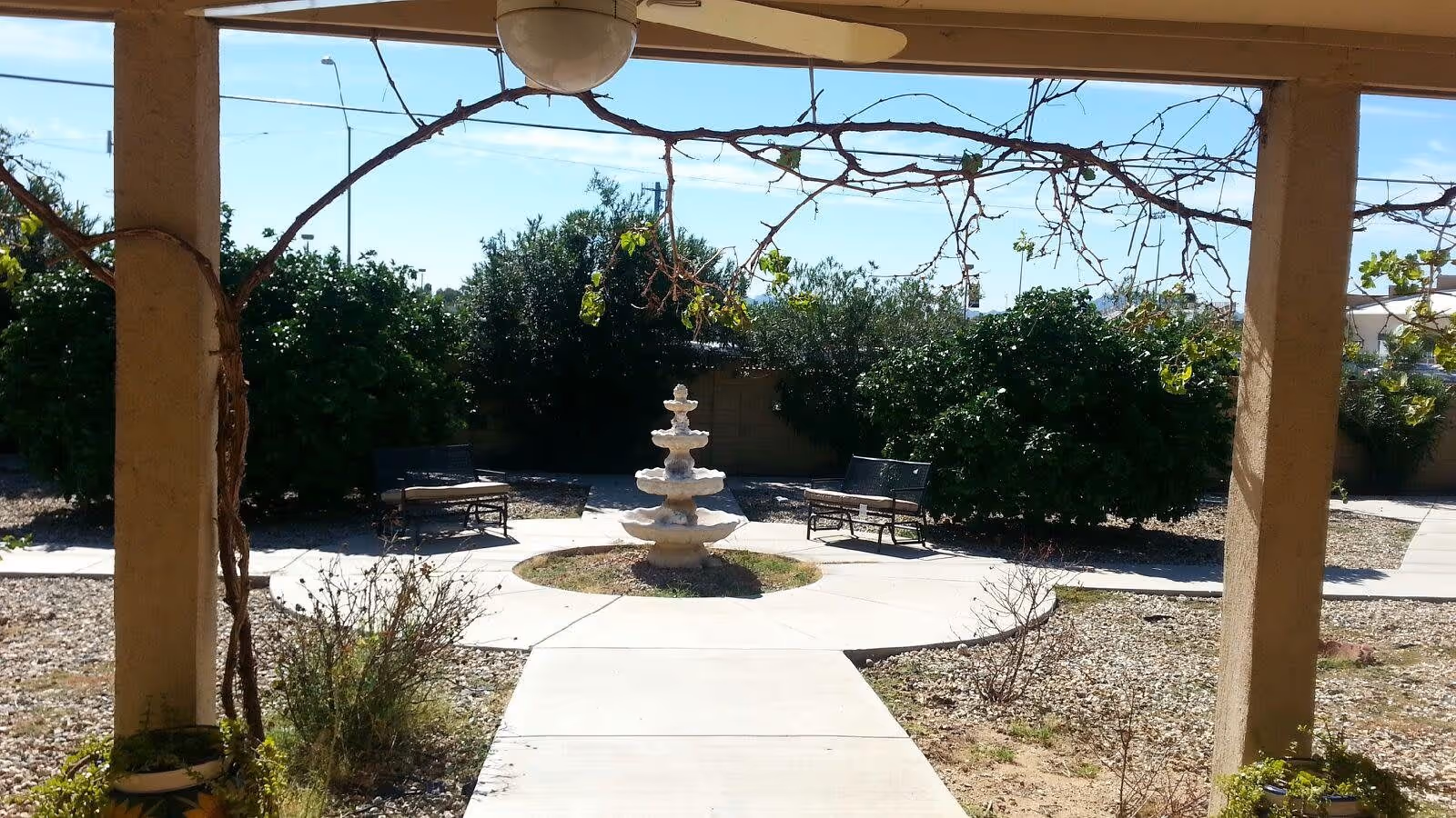 Covered outdoor courtyard with a central tiered fountain, benches, walkways and surrounding shrubs.