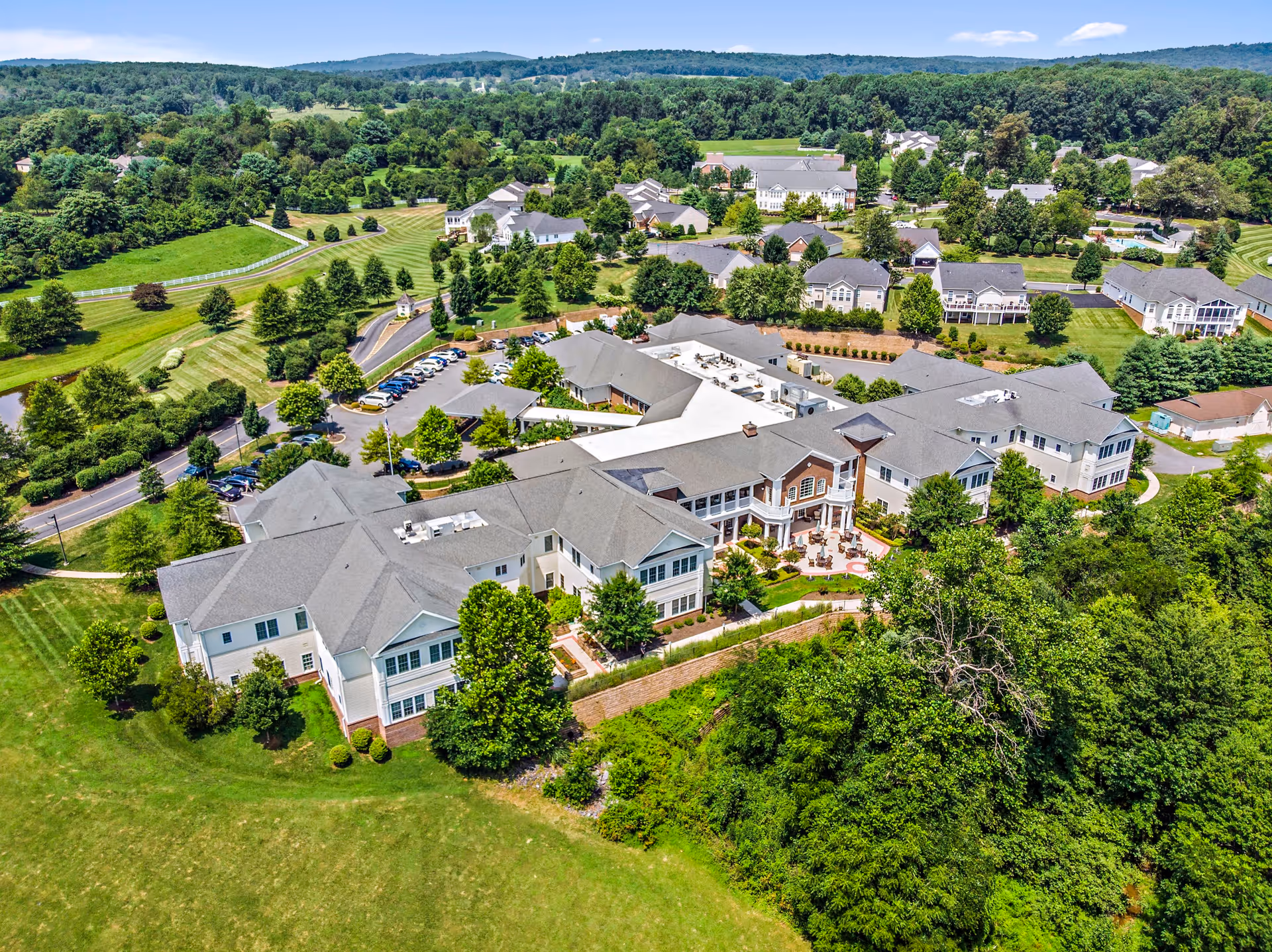 Aerial view of The Villa at Suffield Meadows senior living facility surrounded by green lawns, trees, and residential houses in the background under a clear blue sky.