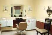 Salon-style interior with a barber chair, hair-washing sink, large mirror and cabinets.