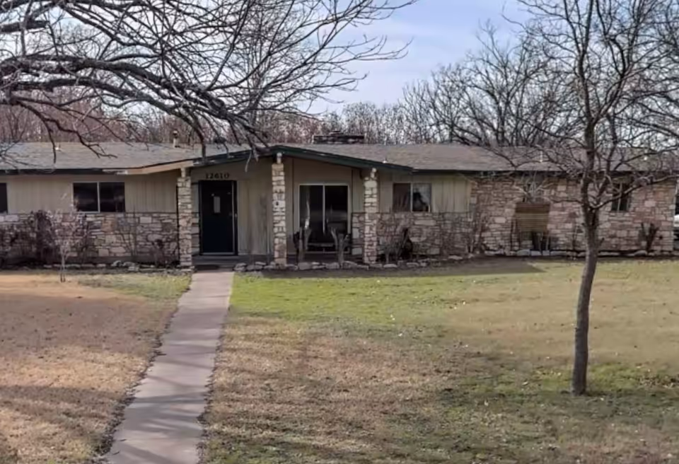 Single-story ranch-style building with a stone facade and a walkway leading to the front door in a grassy yard.