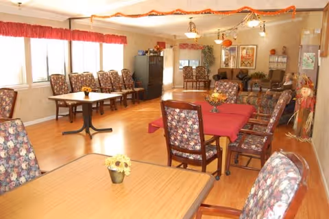 A senior living community dining room with multiple tables, floral-upholstered chairs, couches and seasonal decorations.