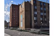 Boardwalk-side exterior view of a multi-story brick nursing facility building with 'Sea Crest' signage and benches along the promenade.