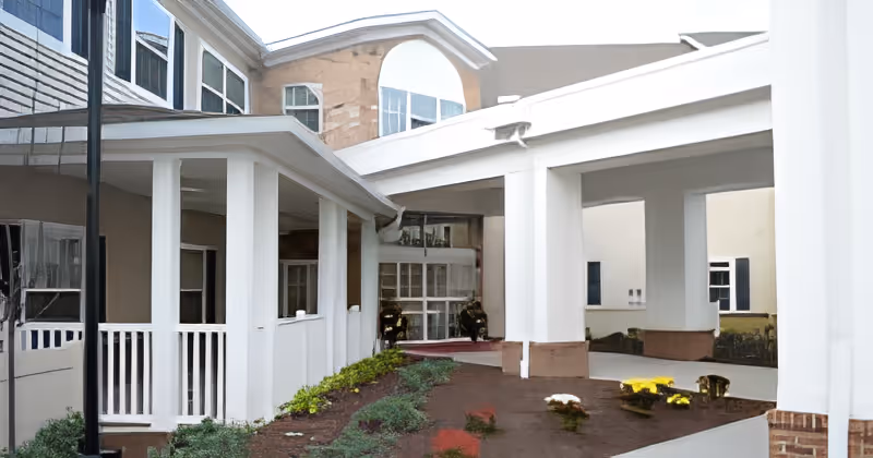 Covered entrance and drive-through portico of a multi-story senior living building with white columns and landscaped beds.