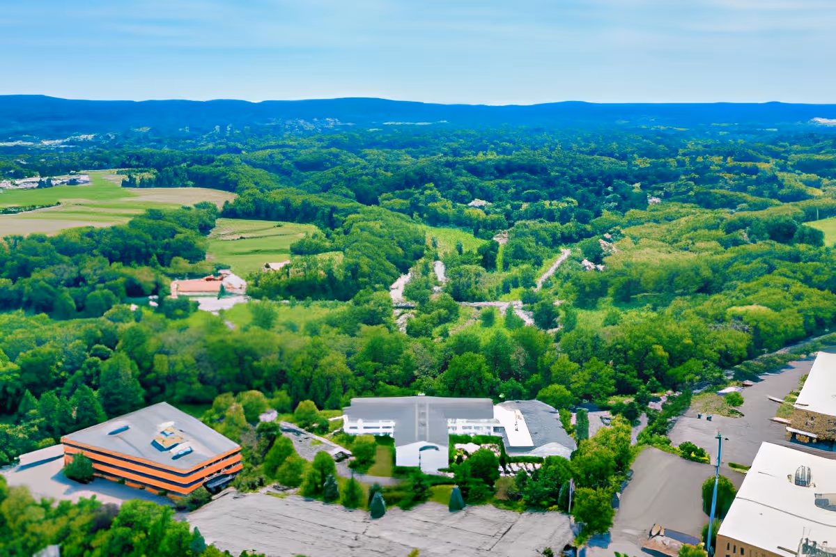 Aerial view showing a wooded landscape with roads and several campus buildings.