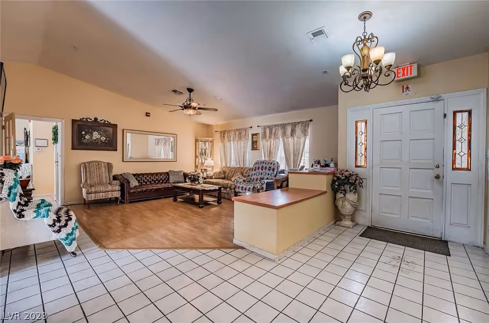 Bright senior living reception area showing a front door, reception desk, tiled entry and a seating area with sofas and chairs.