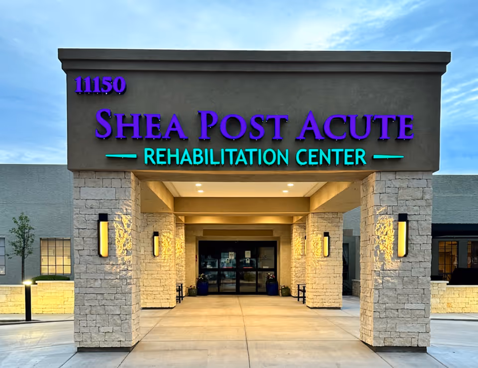 Entrance of Shea Post Acute Rehabilitation Center with stone pillars and illuminated signage displaying the facility name and address number 11150.