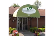 Exterior view of Elmwood Nursing and Rehab entrance with a green awning and potted plants.