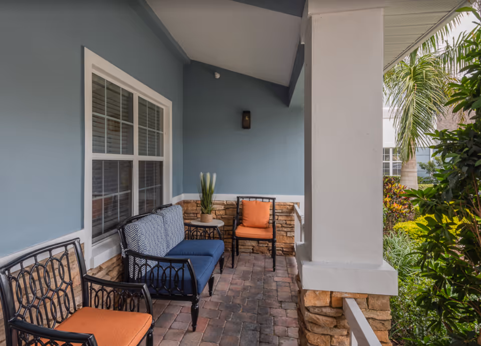 Covered front porch with blue walls, a white column and stone base, and outdoor seating with orange and blue cushions.