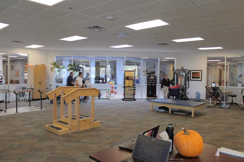 Large open rehabilitation and exercise room with therapy equipment, staff and a pumpkin on a foreground desk.