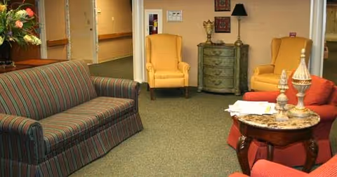 Common area lounge with a striped sofa, upholstered armchairs, side tables and a hallway in the background.