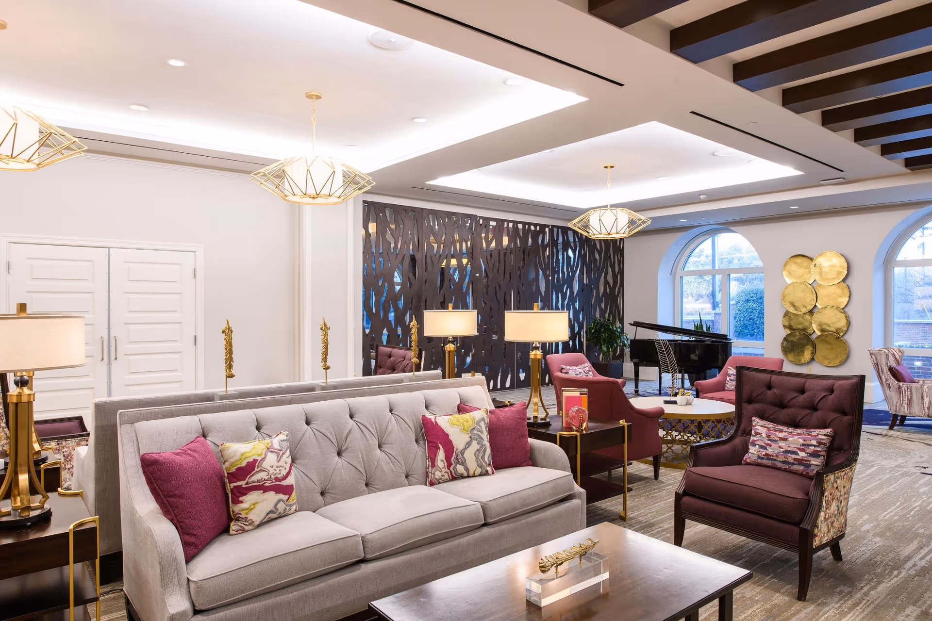 Spacious, elegant common lounge with tufted sofas and armchairs, a grand piano, decorative wall panels, and pendant lighting.