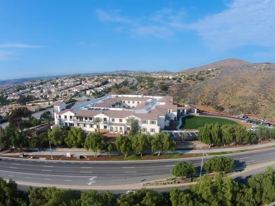 Aerial view of Westmont at San Miguel Ranch senior living facility surrounded by trees, roads, and hills under a blue sky.