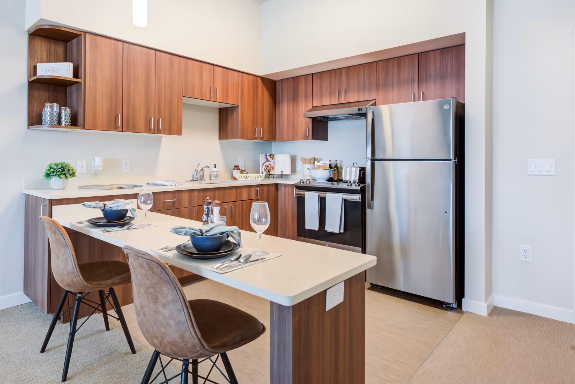 Modern kitchen with wood cabinets, stainless steel refrigerator and stove, and a breakfast bar set for two.