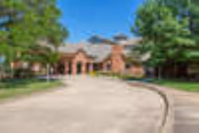 Front exterior view of a brick building with a curved driveway and green trees on both sides under a clear blue sky.