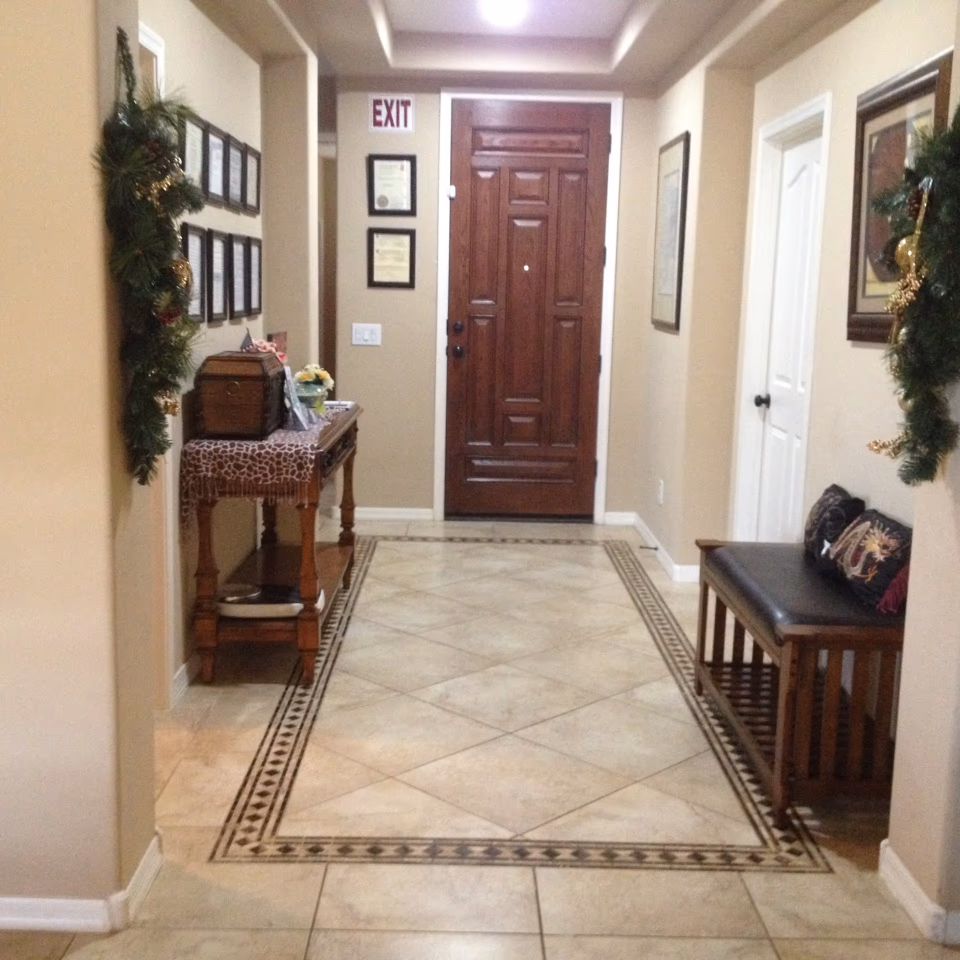 A decorated hallway entry with a wooden front door, patterned tiled floor, side table and bench.