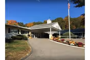 Front entrance of Norwichtown Rehabilitation & Healthcare with a covered porte-cochere, driveway, landscaped flower beds and an American flag.