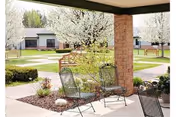Covered patio with metal chairs overlooking a landscaped courtyard with flowering trees and single-story buildings.