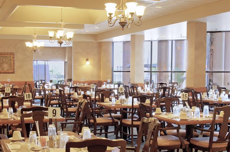 Spacious dining room with many set tables and chairs, numbered place settings, and large windows.