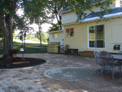 Yellow house-style senior living facility with brick-paved patio and outdoor seating.
