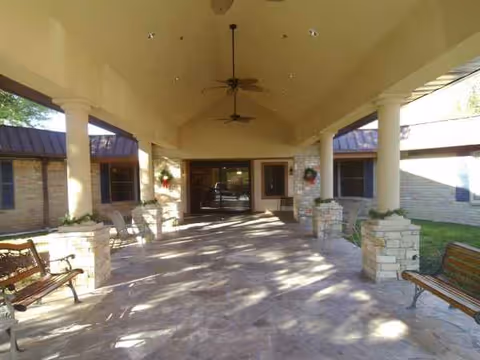 Covered outdoor entrance patio with benches, columns, and ceiling fans; doors in background.