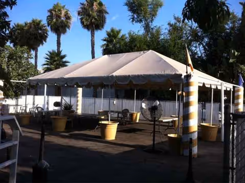 Large white tent set up outdoors with chairs, potted plants, and striped support columns.