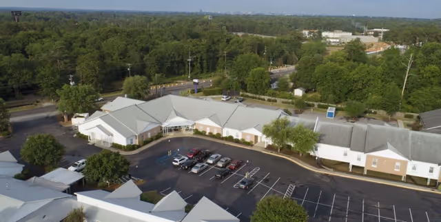 Aerial view of a single-story rehabilitation facility with a central parking lot, parked cars, and surrounding trees.