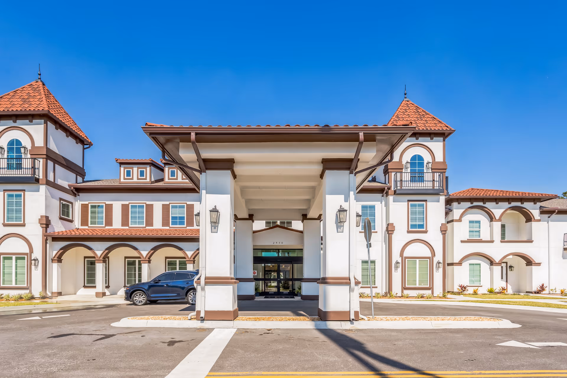 Mediterranean-style building front with a covered porte-cochère, arched windows, and a parked car.