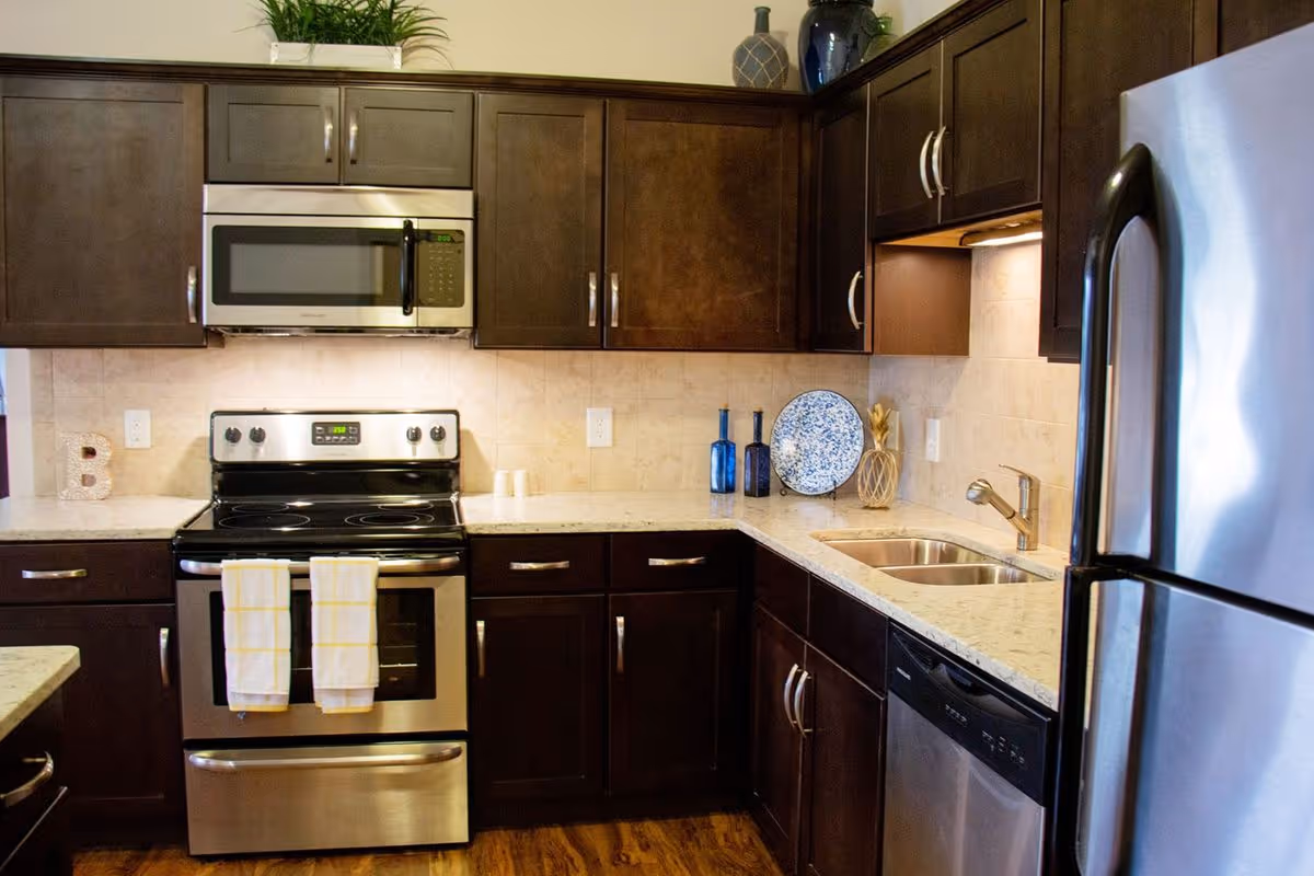 Modern kitchen with dark wood cabinets, stainless steel stove, microwave, refrigerator and dishwasher, and a double sink on a light countertop.