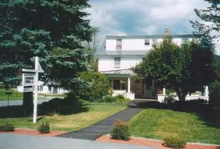 White two-story senior living facility with a front entrance and well-kept lawn