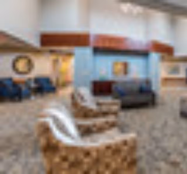 Spacious senior living facility common room with armchairs and sofas arranged around a central column and a decorative wall.
