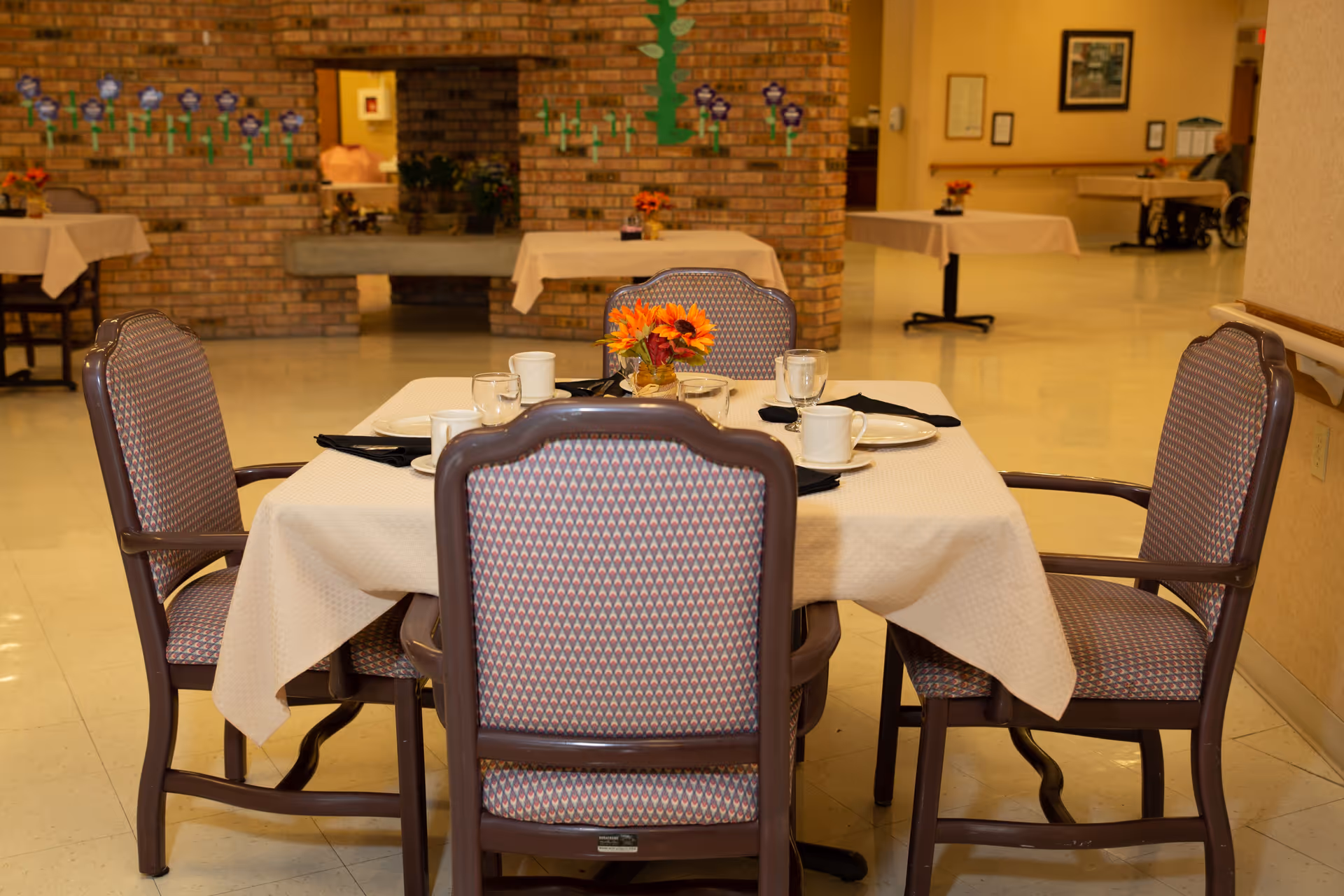 A table set for four with plates, cups and a small floral centerpiece in a senior living dining room.