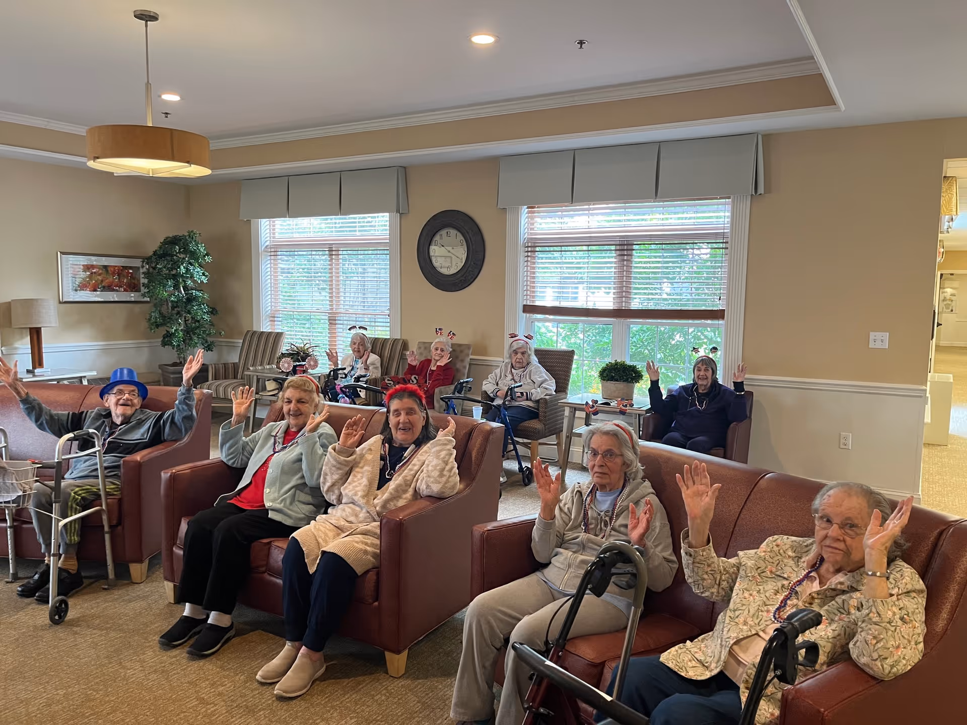A group of seniors in a lounge area smiling and waving their hands.
