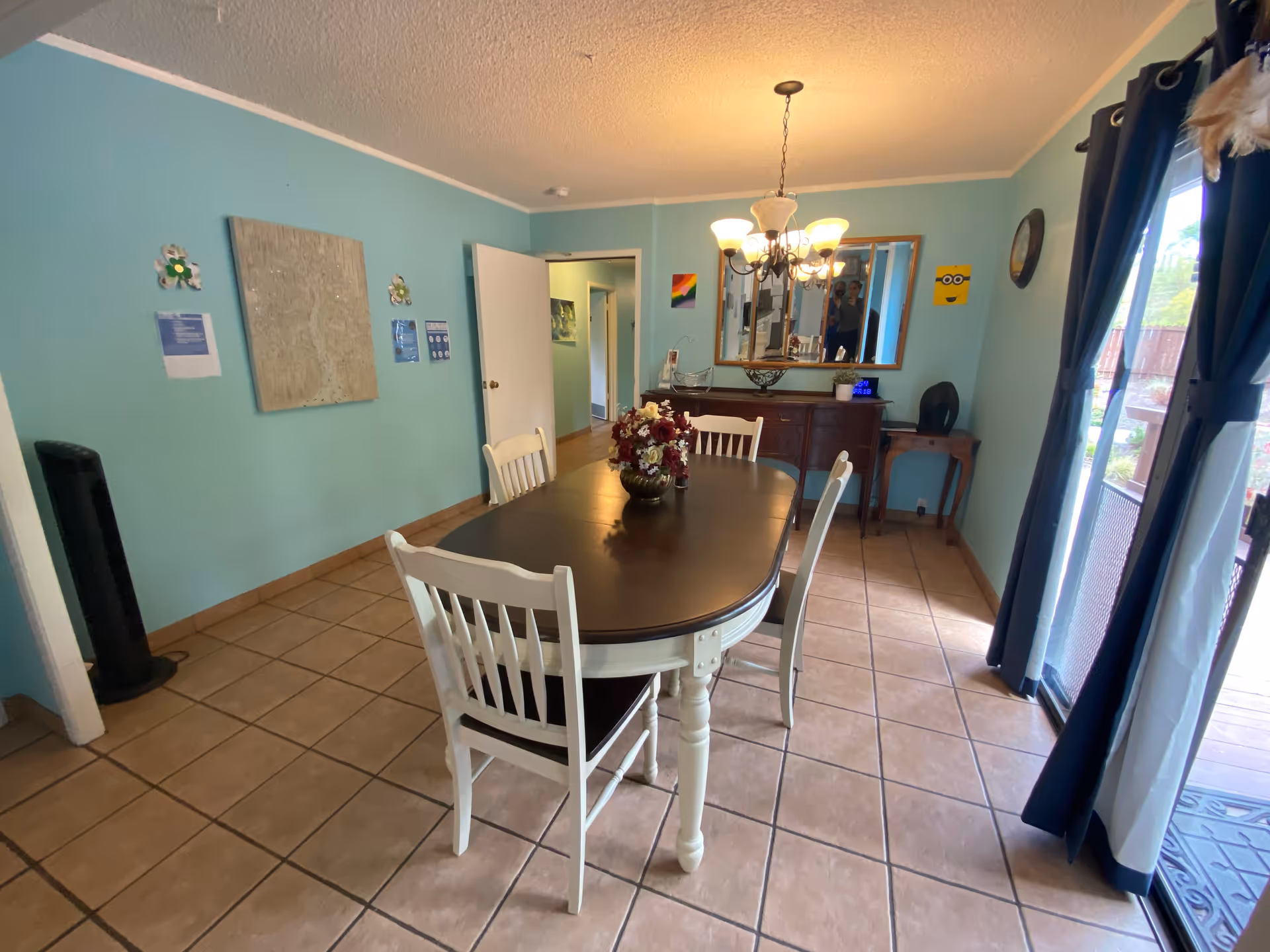 Teal-walled dining room with a dark oval table, white chairs, chandelier, and sliding doors.