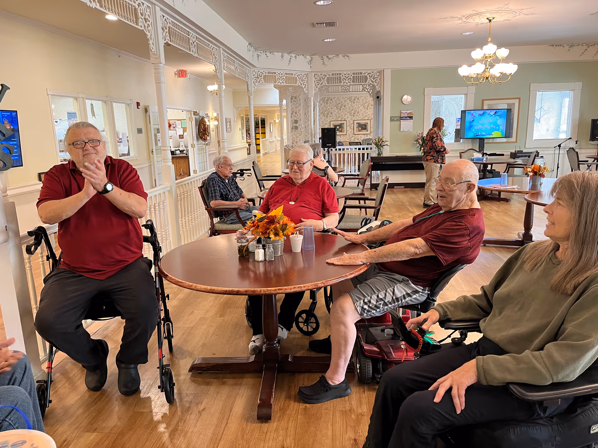 Several elderly residents sitting around a round table in a bright communal room at a senior living facility.