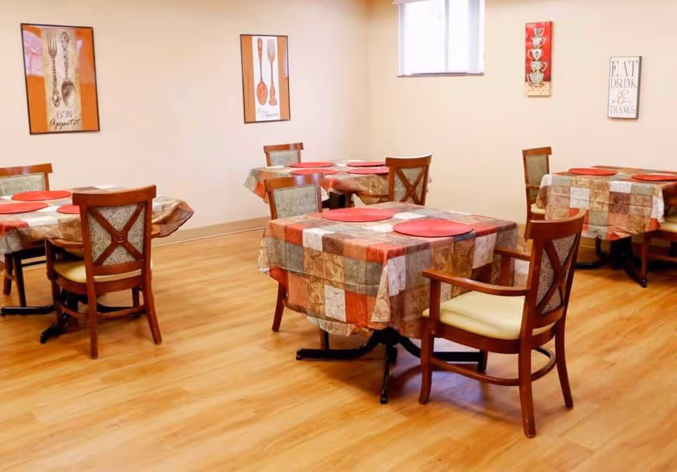 A small dining room with multiple square tables covered in patchwork tablecloths and wooden chairs on a wood floor.